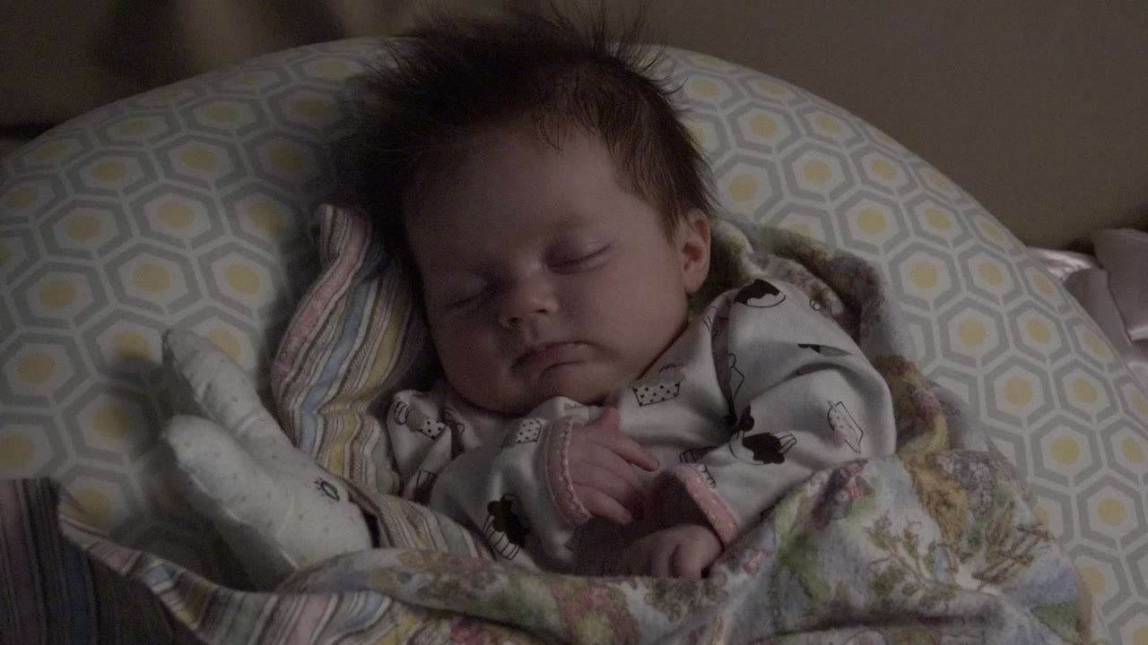 Baby asleep with blanket and patterned cushion around the head.