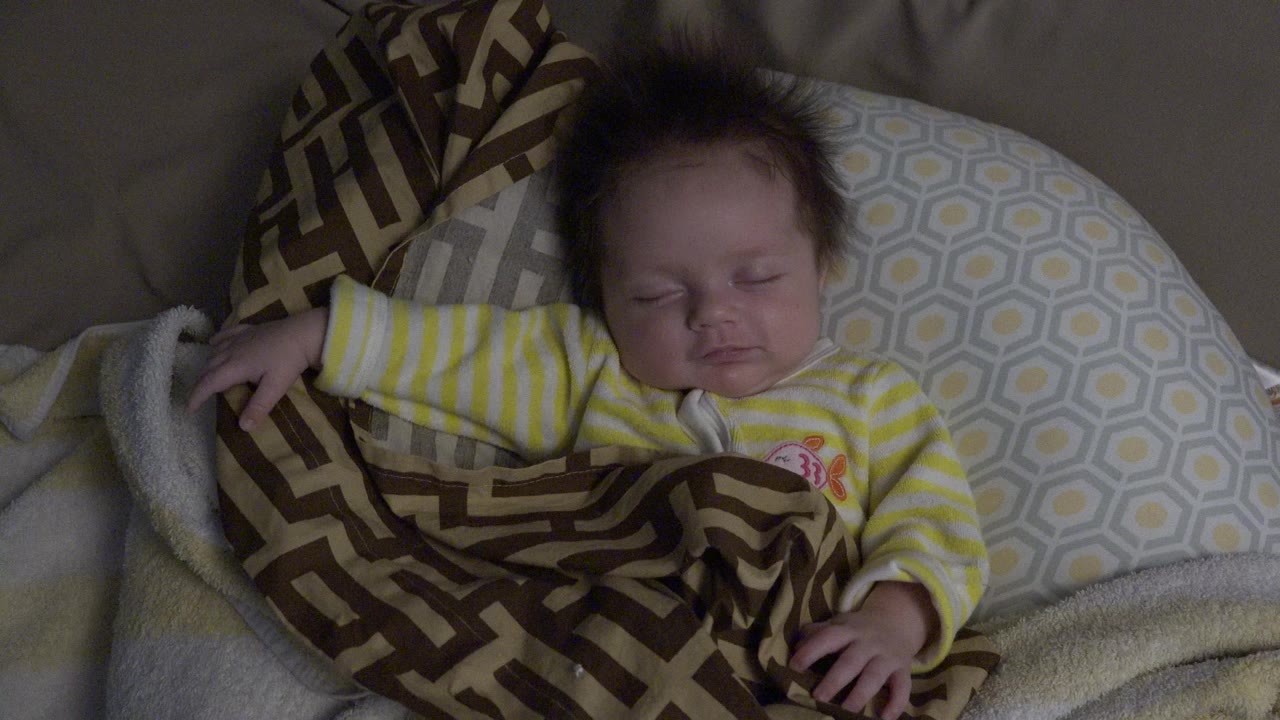Sleeping baby in a yellow striped outfit on pillows and blankets.