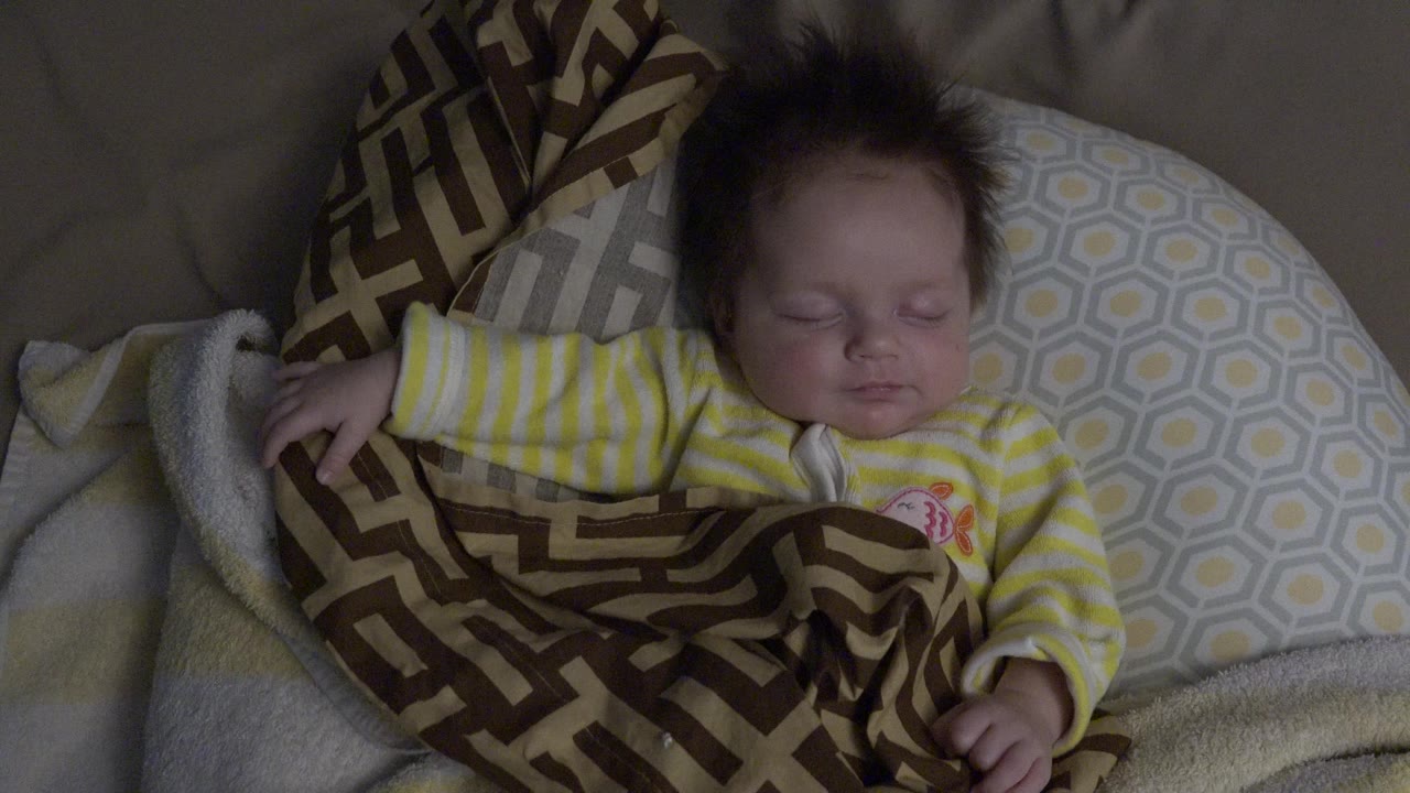 Newborn baby sleeping on pillows under a patterned blanket.