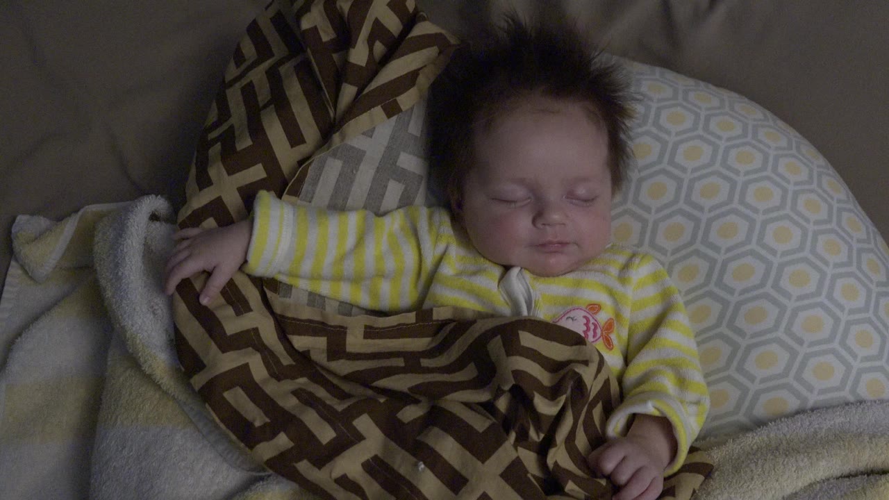 One second into the clip, the newborn remains asleep in a yellow and white striped outfit beside a gray patterned pillow in Westminster, Colorado.