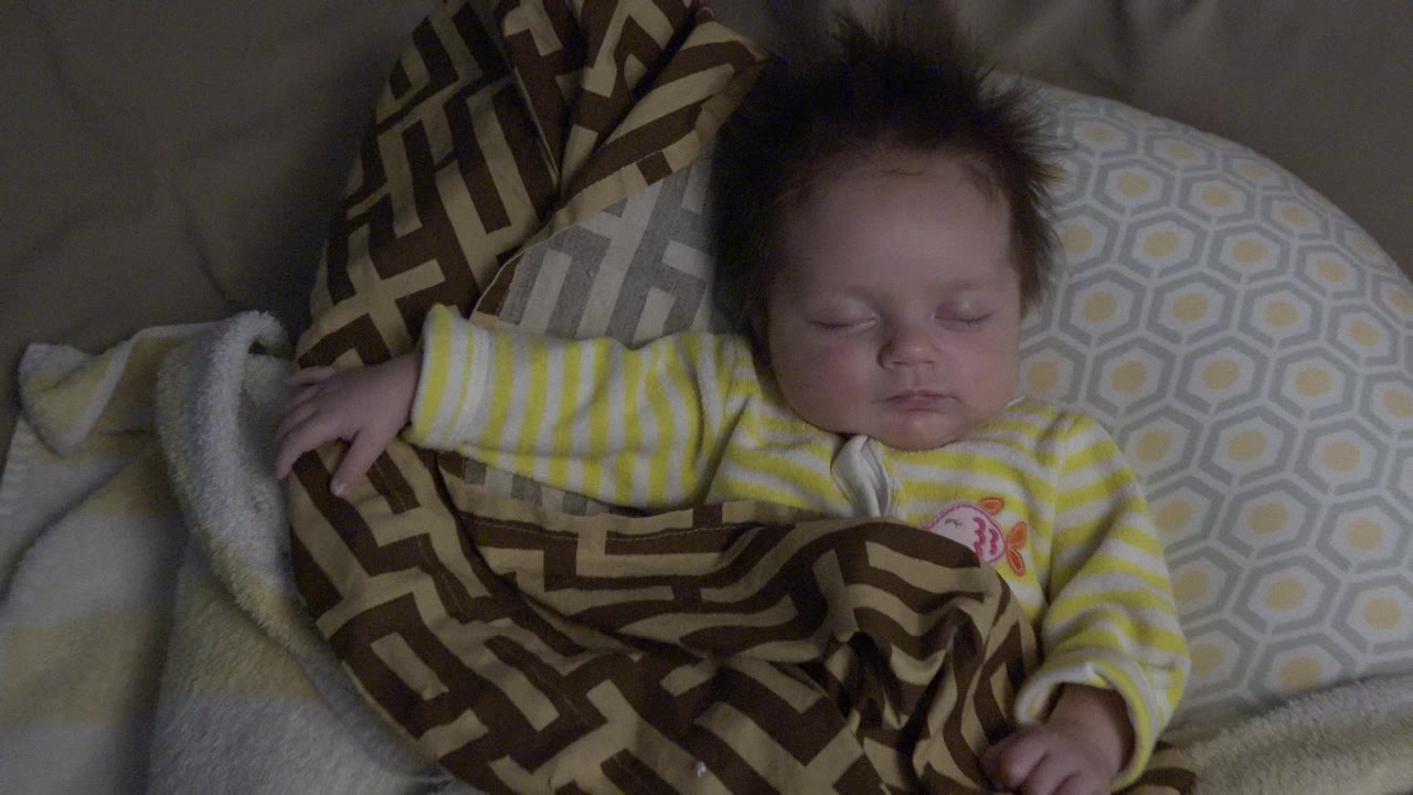 Sleeping baby under a patterned blanket on pillows.