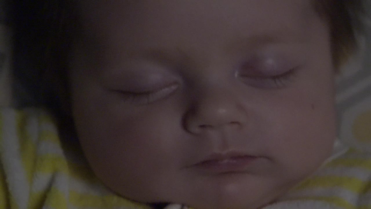 Close-up of a sleeping baby's face in Westminster, Colorado, with closed eyes, dark hair at the edge of frame, and yellow striped clothing visible below.