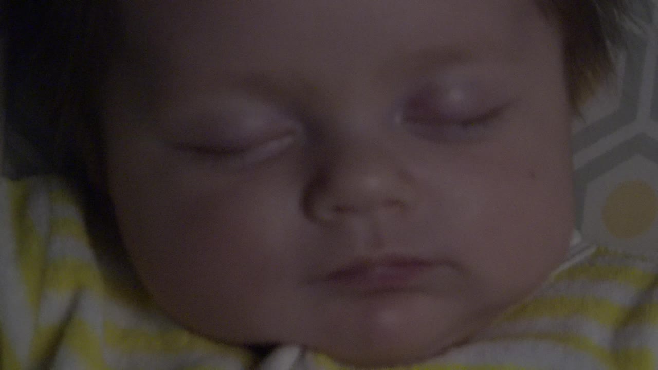 Close infant sleeping portrait with patterned bedding at the side.