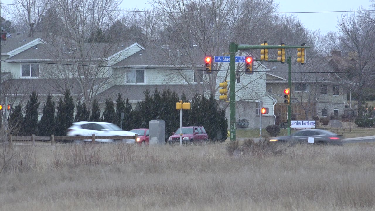 Cars near a red-light intersection with houses and bare trees behind them.