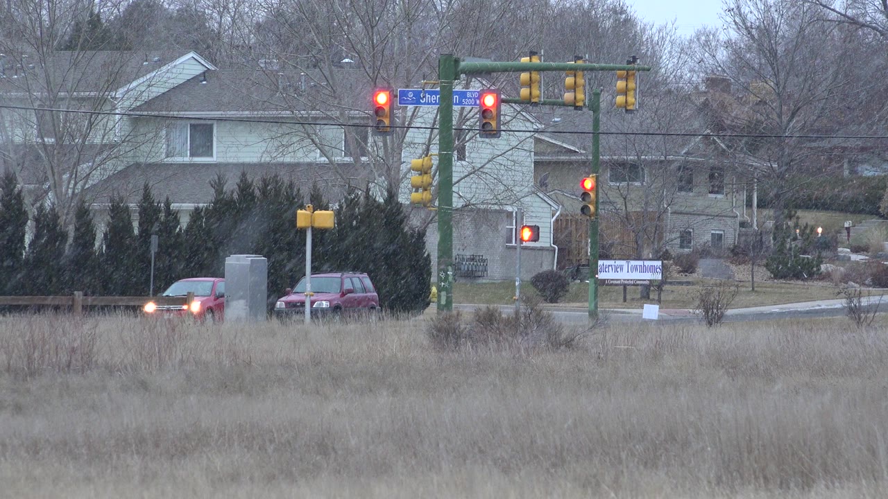 Cars stopped near traffic lights beyond a grassy winter field.