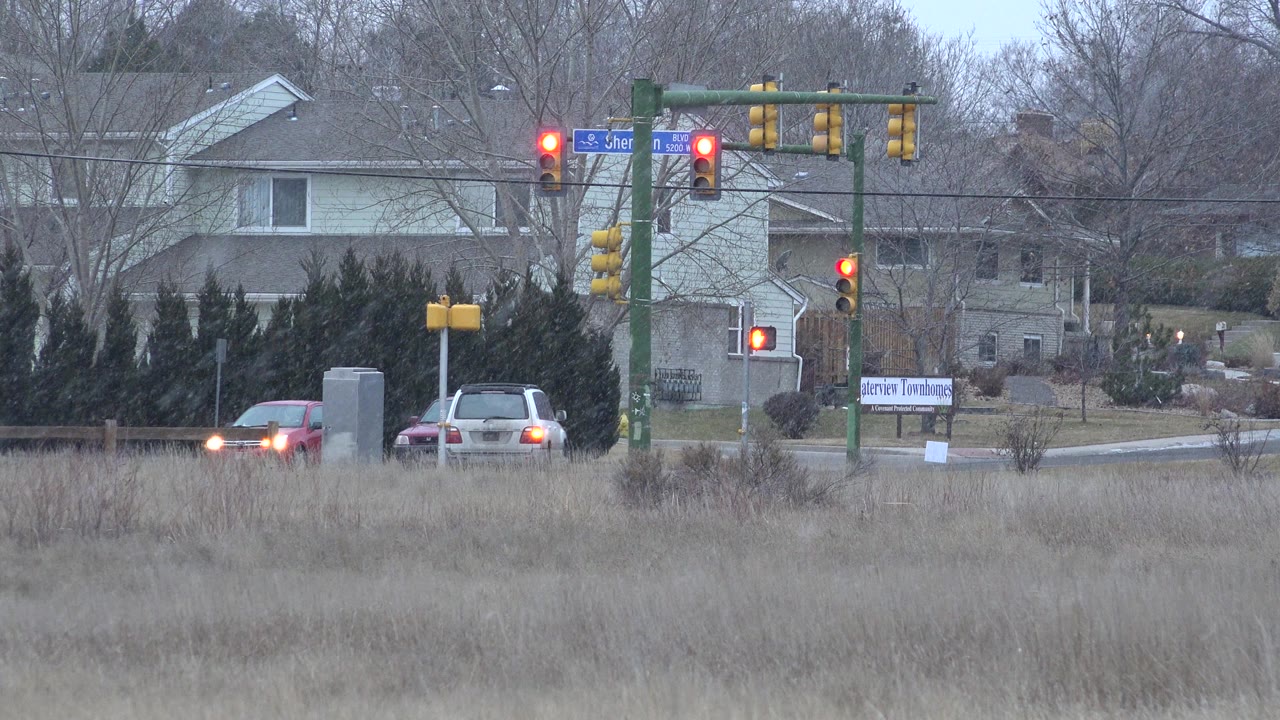 Cars near a red-light intersection behind winter grass.