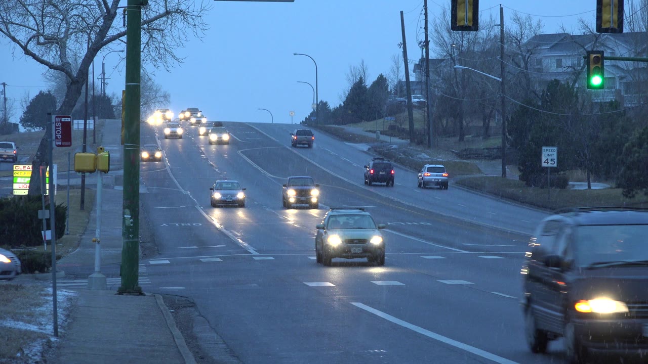 At 0:01 in Westminster, Colorado, a dark vehicle moves through the foreground while several cars with headlights travel uphill in the background, with no visible people.