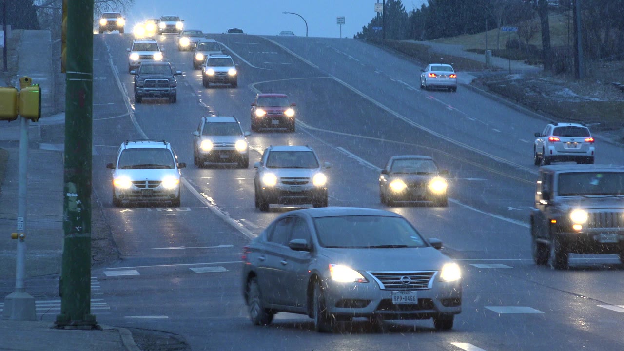 Cars with headlights approach on a wet suburban road at dusk.