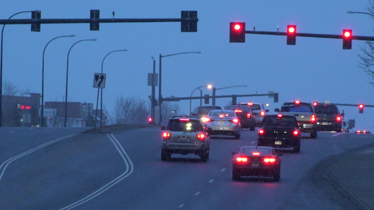 Cars line up on an uphill multi-lane road in Westminster, Colorado, with red traffic signals overhead, blue dusk light, and no visible people.