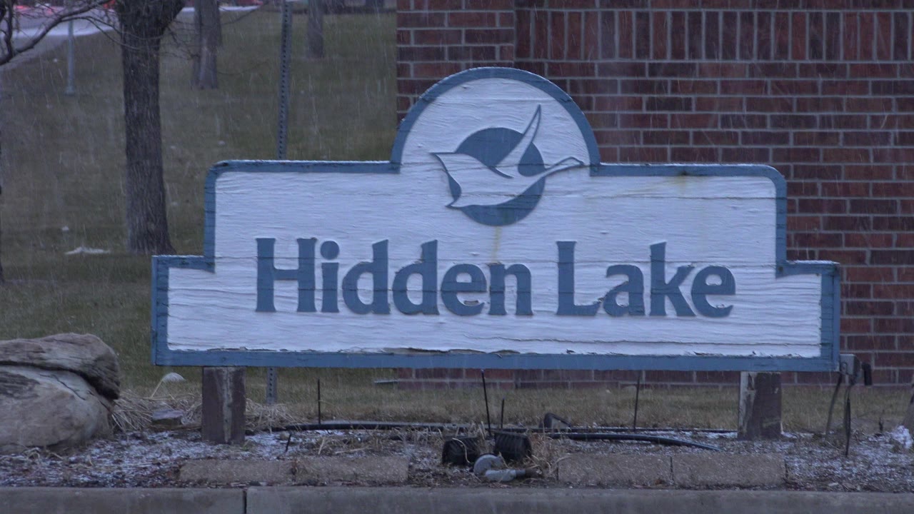 Hidden Lake sign in front of a brick wall and bare trees.
