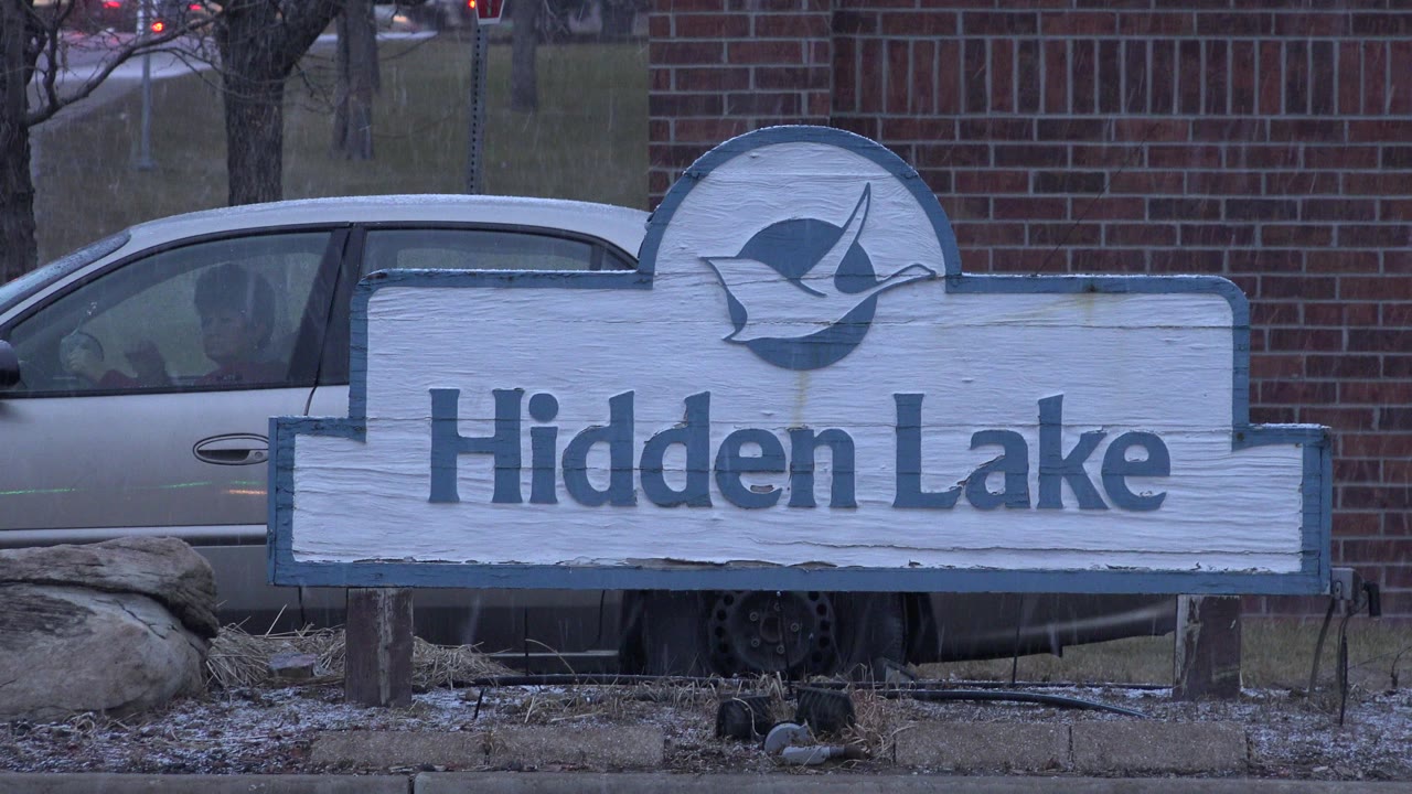 Hidden Lake sign in front of a brick wall and parked car.