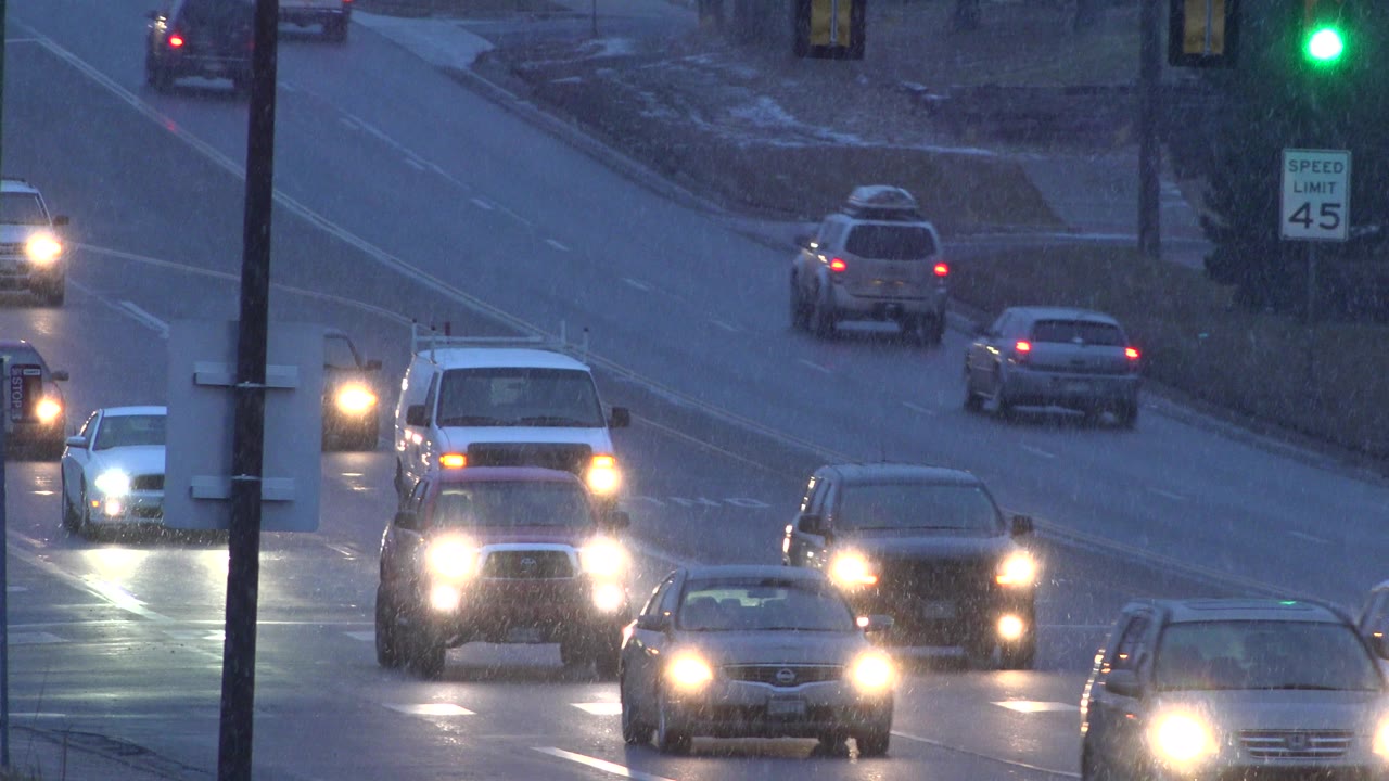 Cars and a pickup truck approach under the green signal on a wet Westminster, Colorado street, with snow along the shoulder and no visible people.