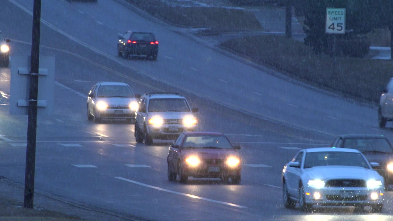 Several cars approach on a wet Westminster, Colorado road under blue evening light, with a roadside speed limit sign and no visible people.