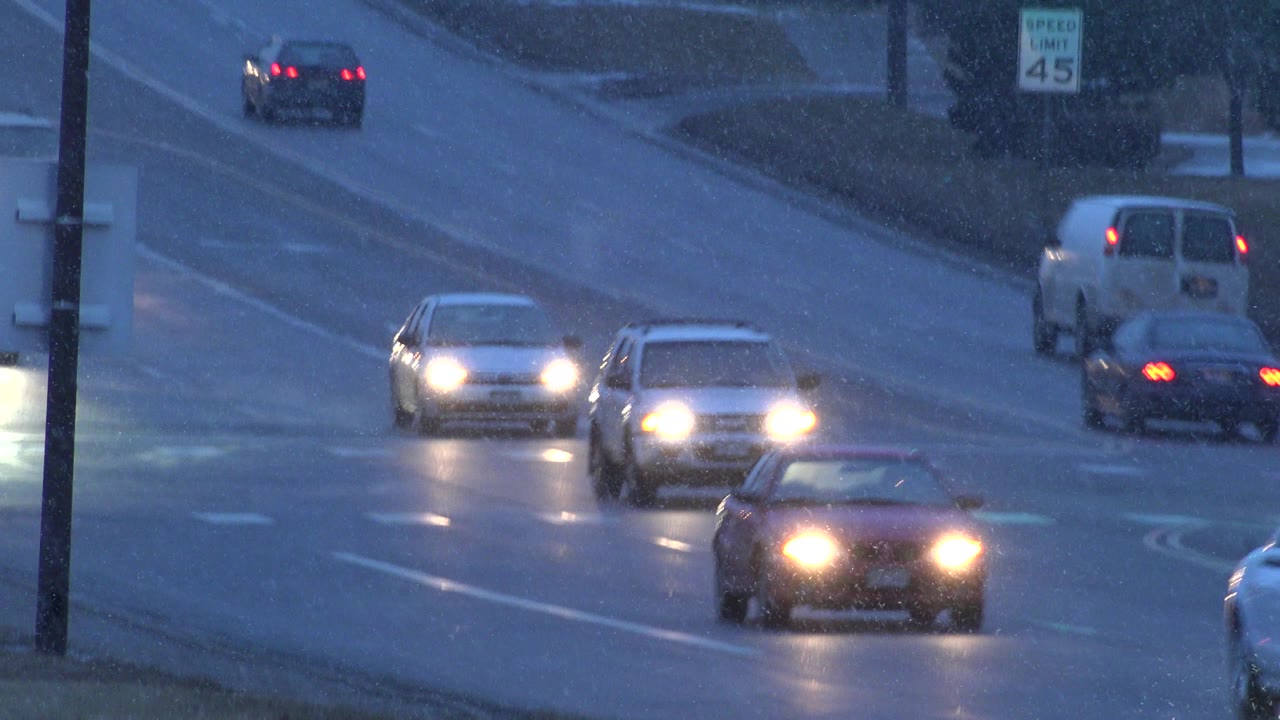 A white van and several cars pass through the Westminster, Colorado street scene as headlights and taillights mark traffic in both directions, with no visible people.