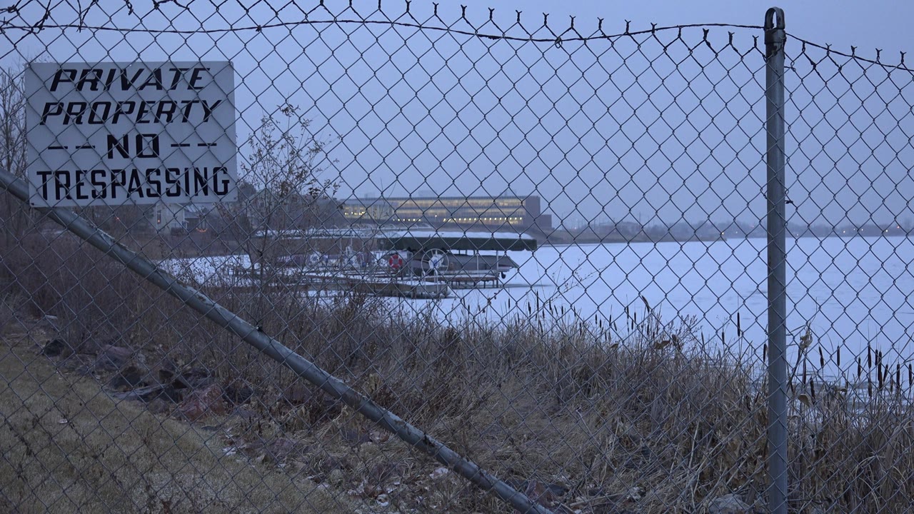 No trespassing sign on chain-link fence near calm lake