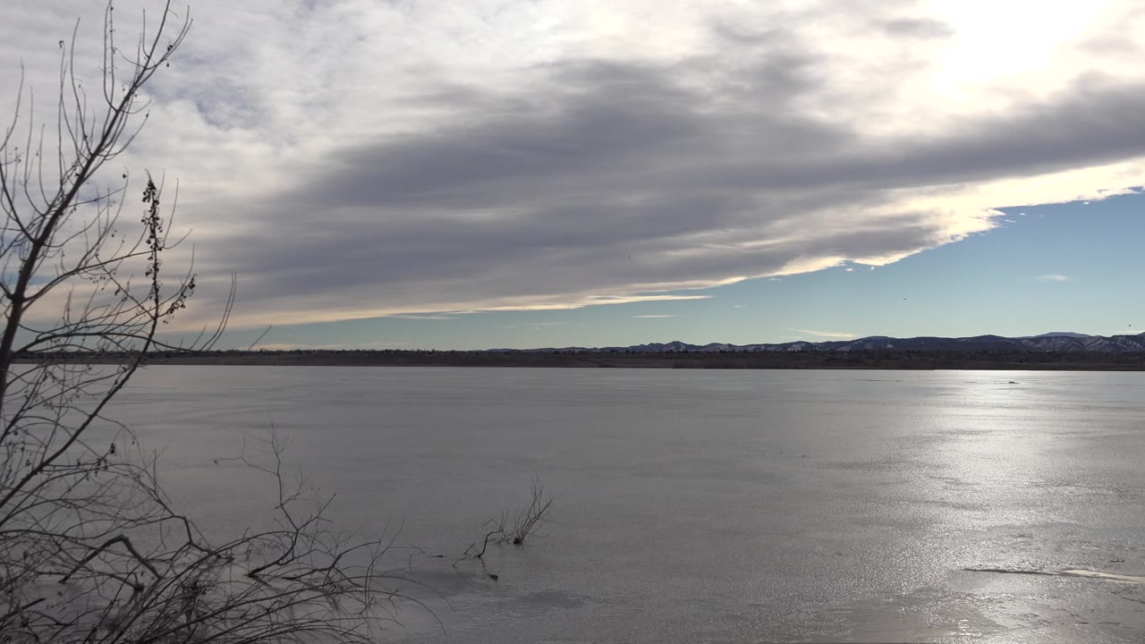 Wide icy water view with clouds, blue sky, and hills.
