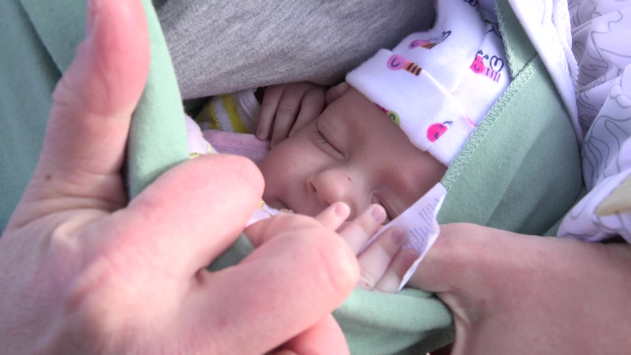 Close view of a newborn sleeping in a green fabric sling.