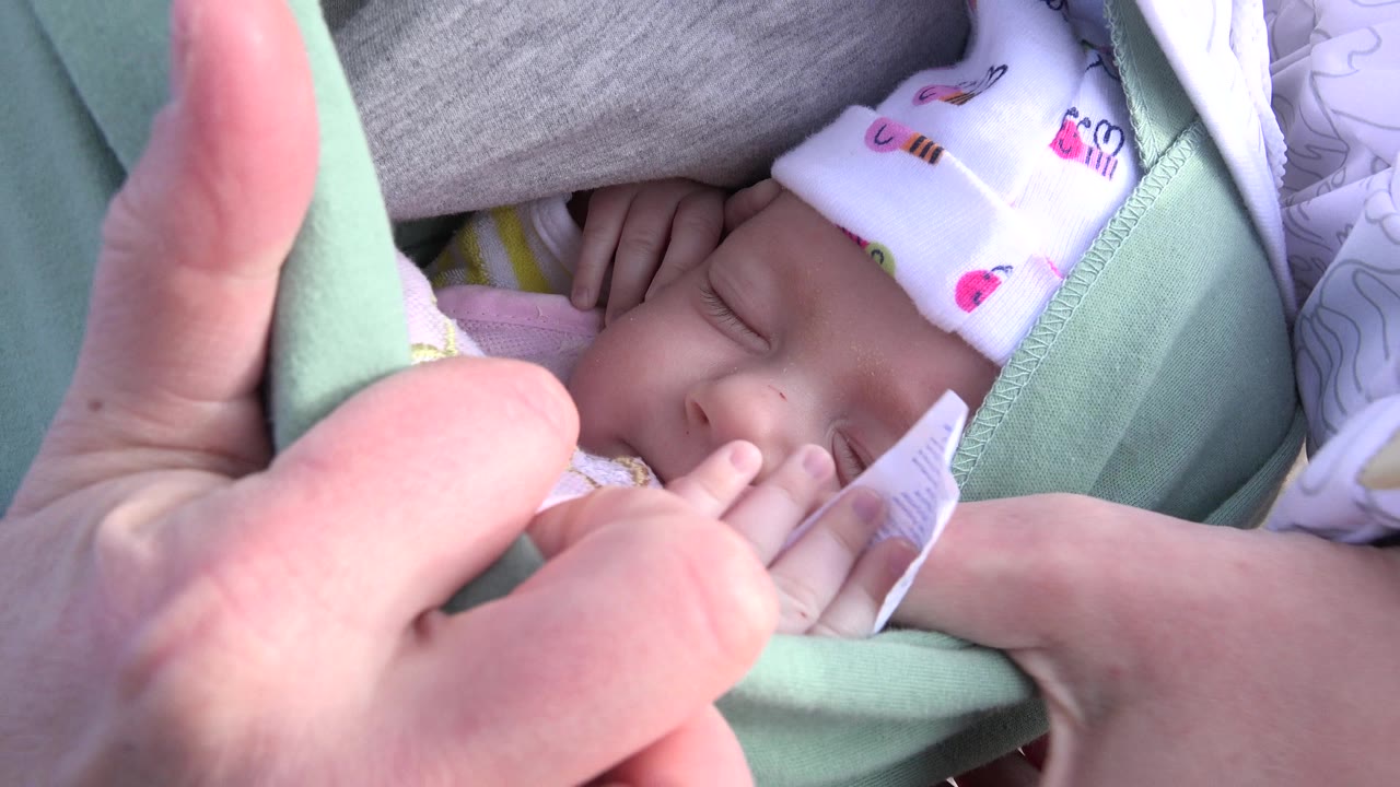 Close Westminster, Colorado frame with an adult hand in the foreground and the newborn's face partly shaded inside the pale green carrier.
