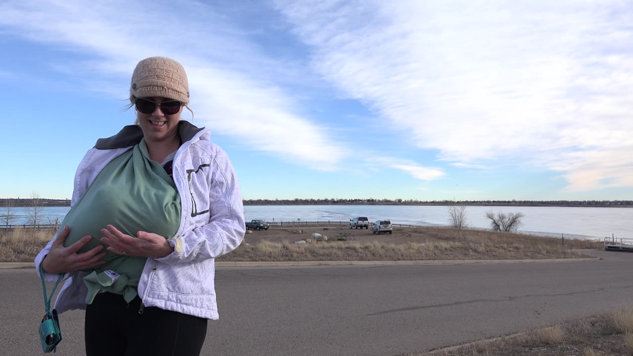 Woman at the roadside with lake, vehicles, and wide cloud cover behind her.