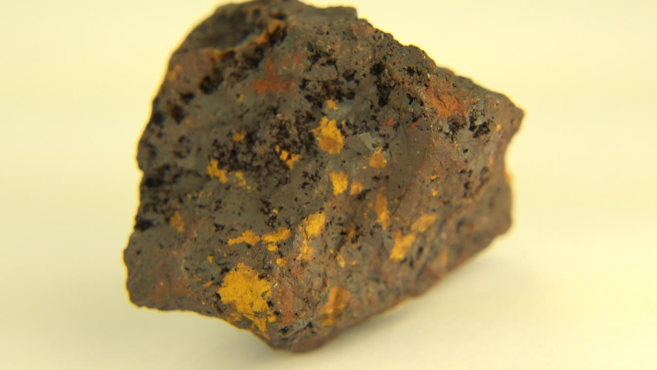 Rough dark rock with ochre mineral spots on a pale background.