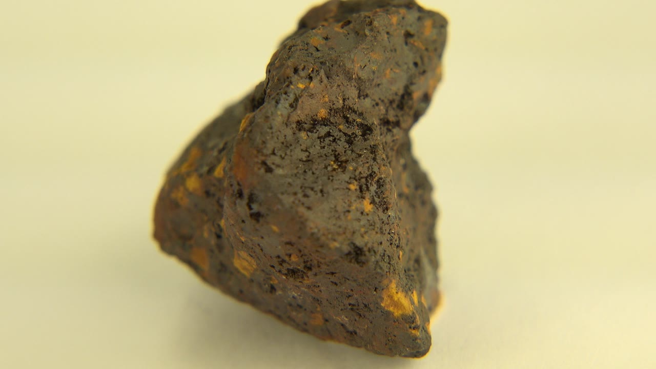 A dark jagged rock with small gold-colored flecks faces slightly left on a pale cream surface in Westminster, Colorado, with no visible people.