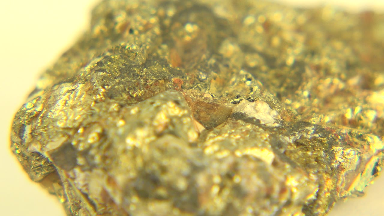 Opening macro frame from Westminster, Colorado showing a rough gold-colored piece with soft focus at the front edge, bright highlights, and no visible people.