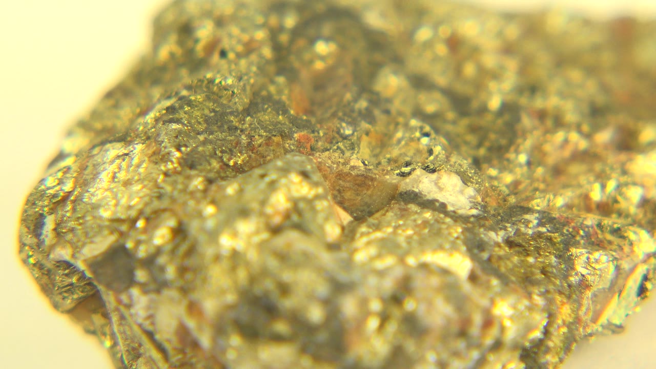 Macro frame from Westminster, Colorado with the gold-colored specimen centered low in frame, reflective flecks across the surface, and no visible people.