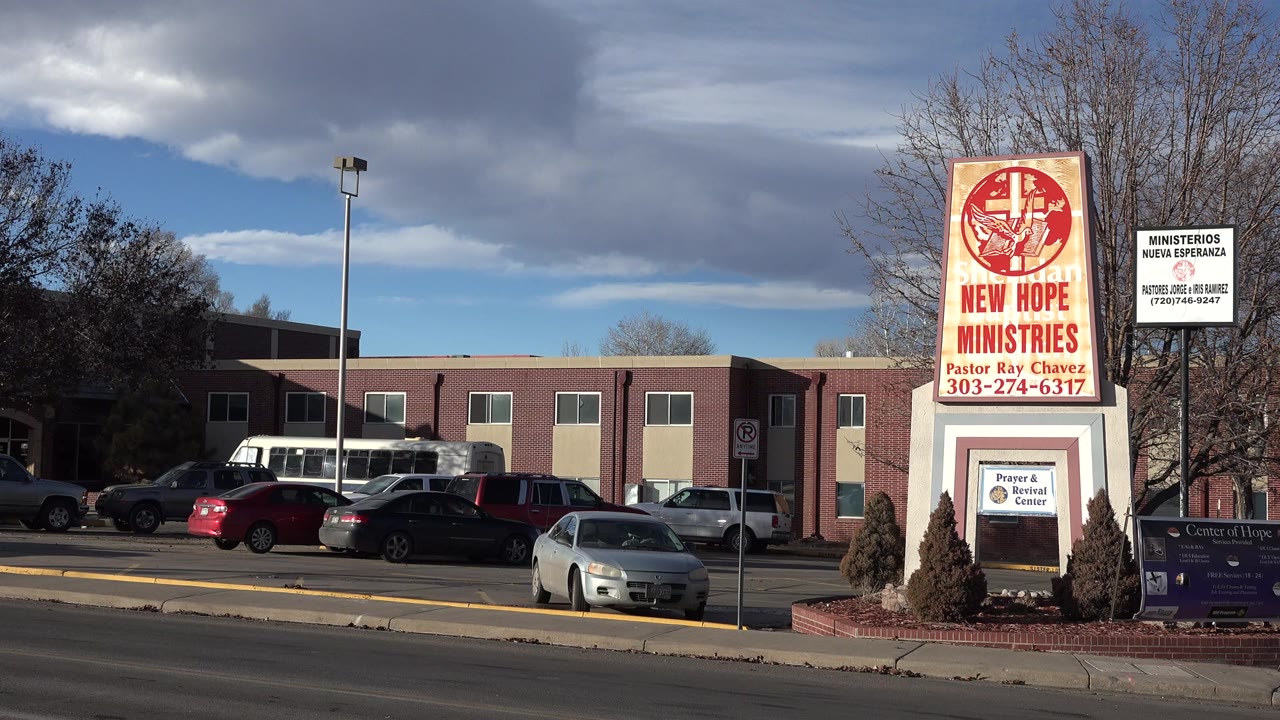 A Westminster, Colorado church or ministry exterior appears across a multi-lane road, with a tall New Hope Ministries sign, parked cars, leafless trees, clouds, and no visible people.