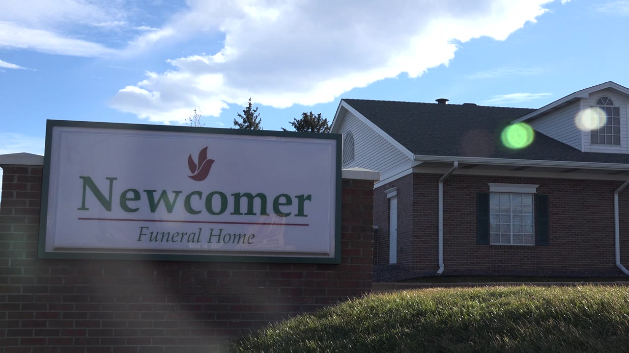The Newcomer Funeral Home sign remains readable at the left of the Westminster exterior, with the brick building and dormer windows behind it and no visible people.