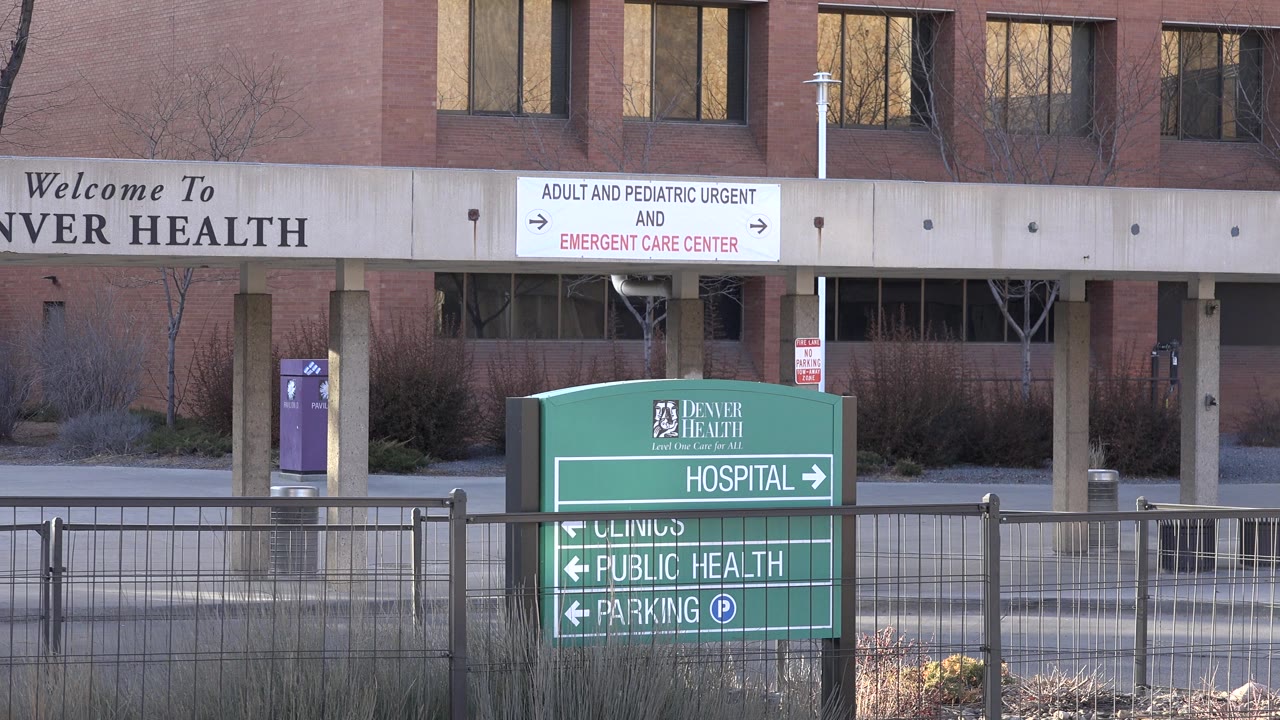 Second frame holds on the green hospital sign in Westminster, Colorado, with the emergency care directional board centered above the entrance canopy and no visible people.