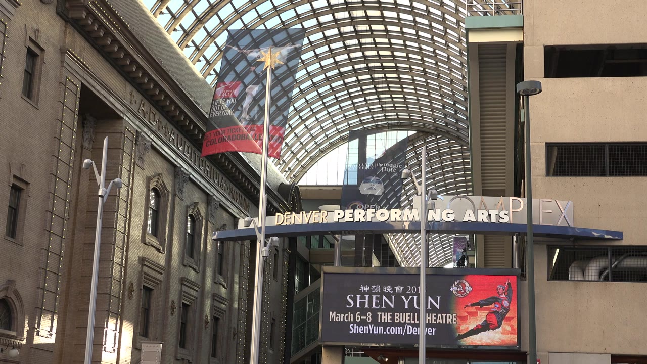 Opening frame of a glass arched roof over building facades in Westminster, Colorado, with Denver Performing Arts signage and no visible people.