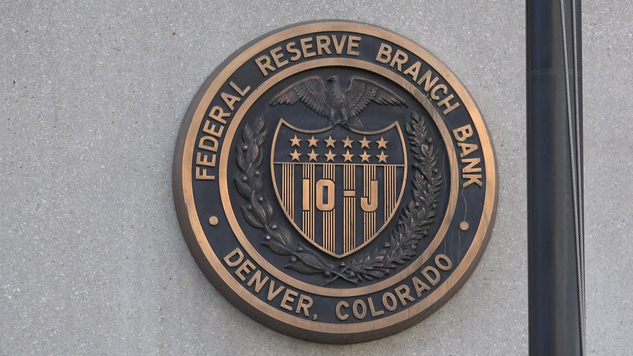 Close view of the Federal Reserve Branch Bank Denver, Colorado seal mounted on a gray exterior wall, with a dark vertical mullion at right and no visible people.