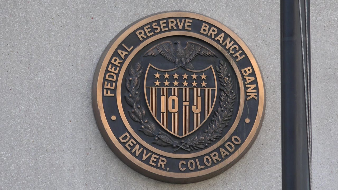 Centered exterior view of the Federal Reserve Branch Bank Denver, Colorado seal against a plain gray facade, with no visible people in frame.