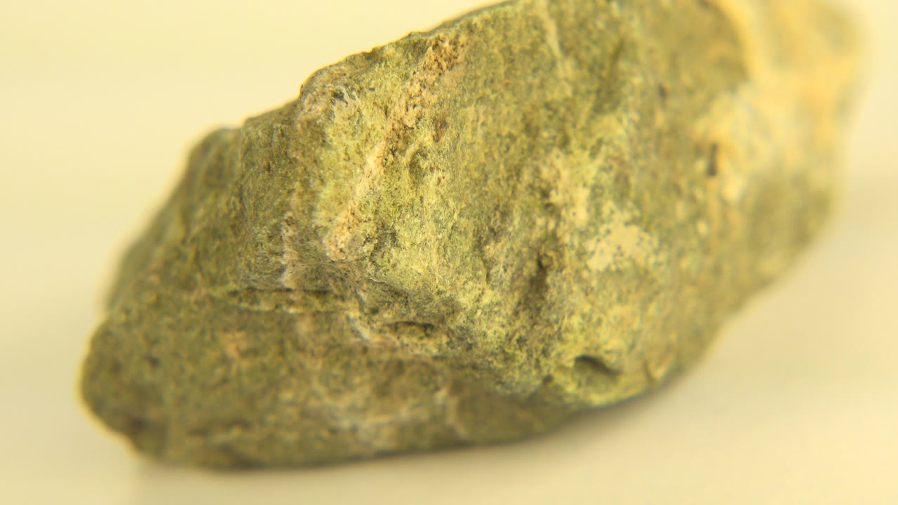 At 0:00, a speckled gray-green rock sits in close-up on a cream tabletop in Westminster, Colorado, with the left end lower in frame and no visible people.