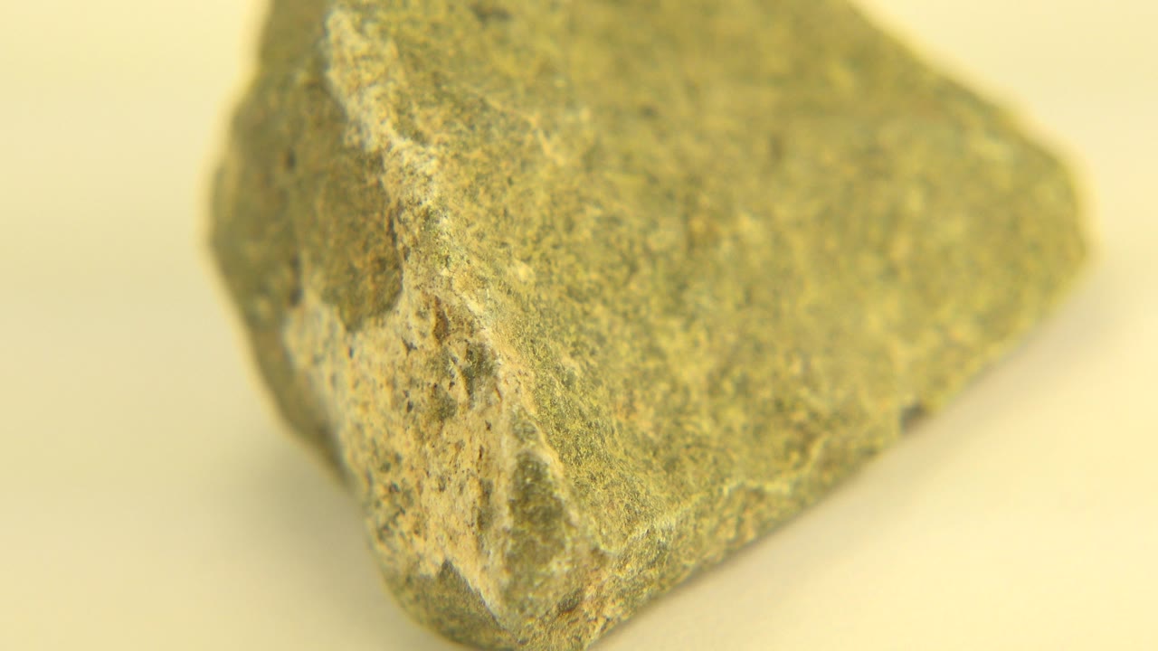 The rock remains tightly framed on a warm pale background, showing a raised ridge and coarse surface texture, with no visible people.