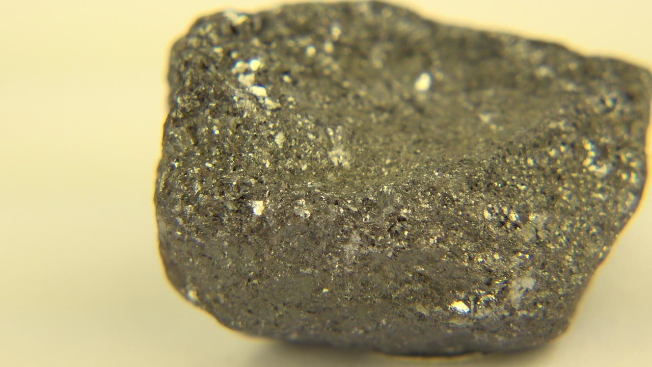 Close-up of a gray, rough-surfaced rock with bright flecks on a pale yellow background in Westminster, Colorado, with no visible people.