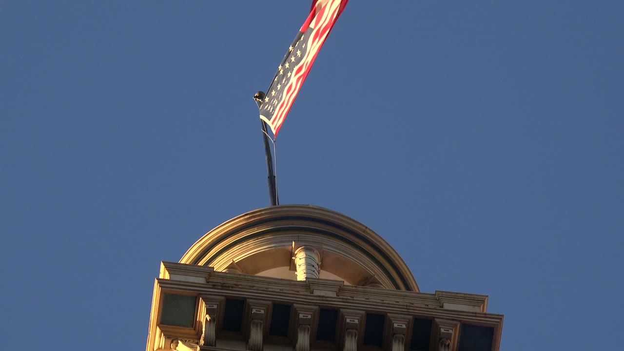 In Westminster, Colorado, the American flag bends in the wind above a rounded rooftop detail on a brick building, with no visible people.