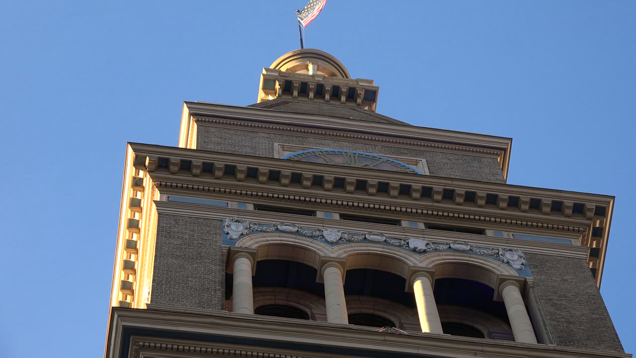 Low-angle view of a Westminster, Colorado government building tower with arched openings, warm side light, and an American flag above the roof, with no visible people.