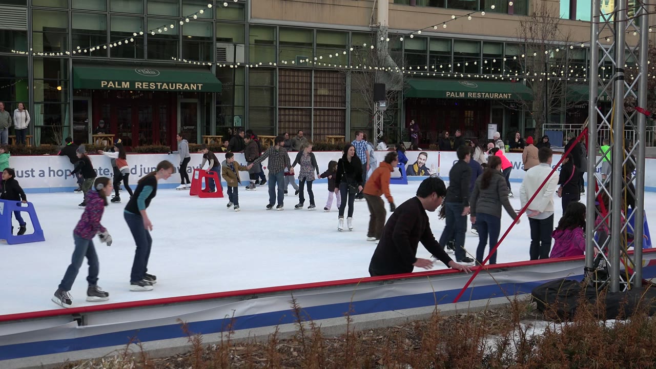 People skate across the Westminster, Colorado rink as a child in pink sits near the red barrier, with blue skate aids and restaurant signage in the background.