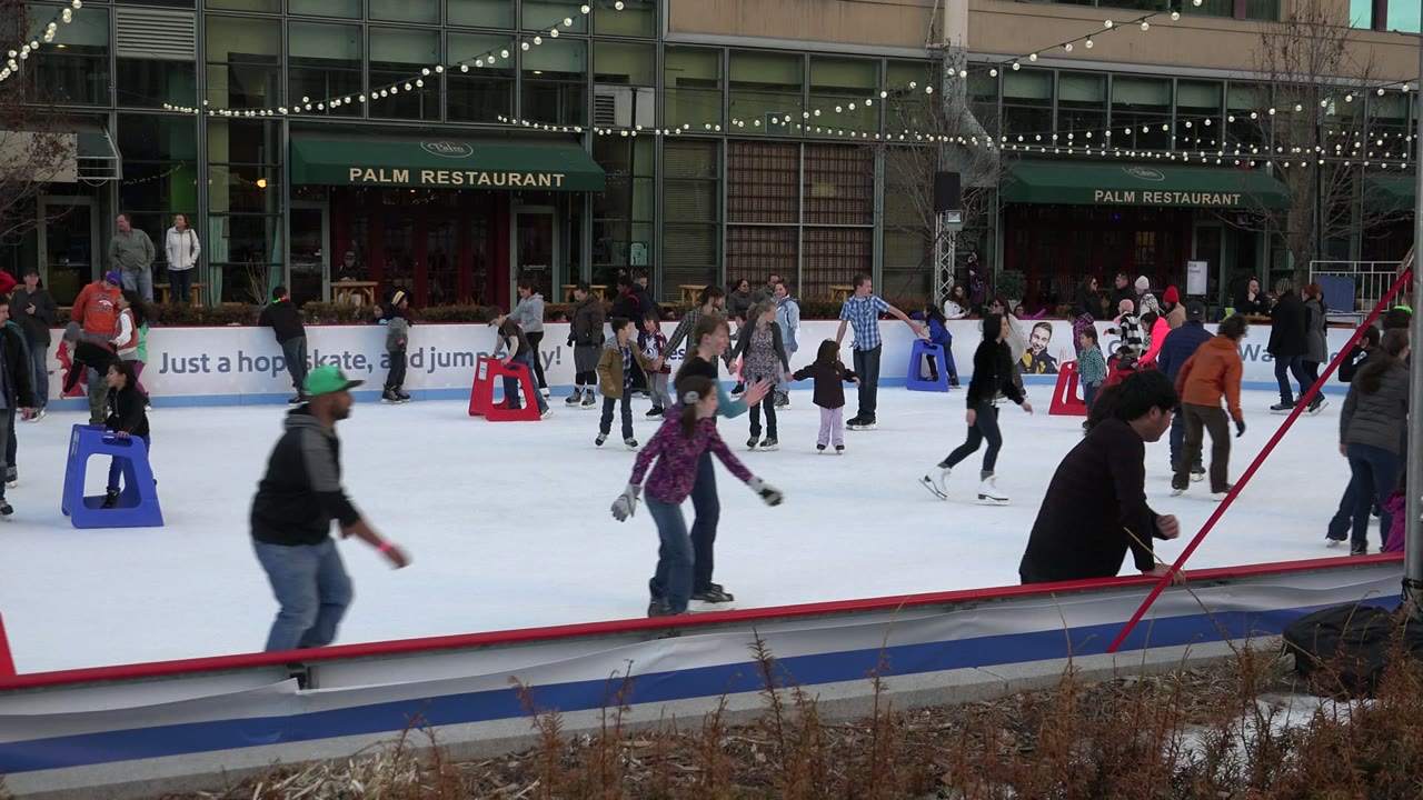 Crowded ice rink with people skating past red and blue supports.