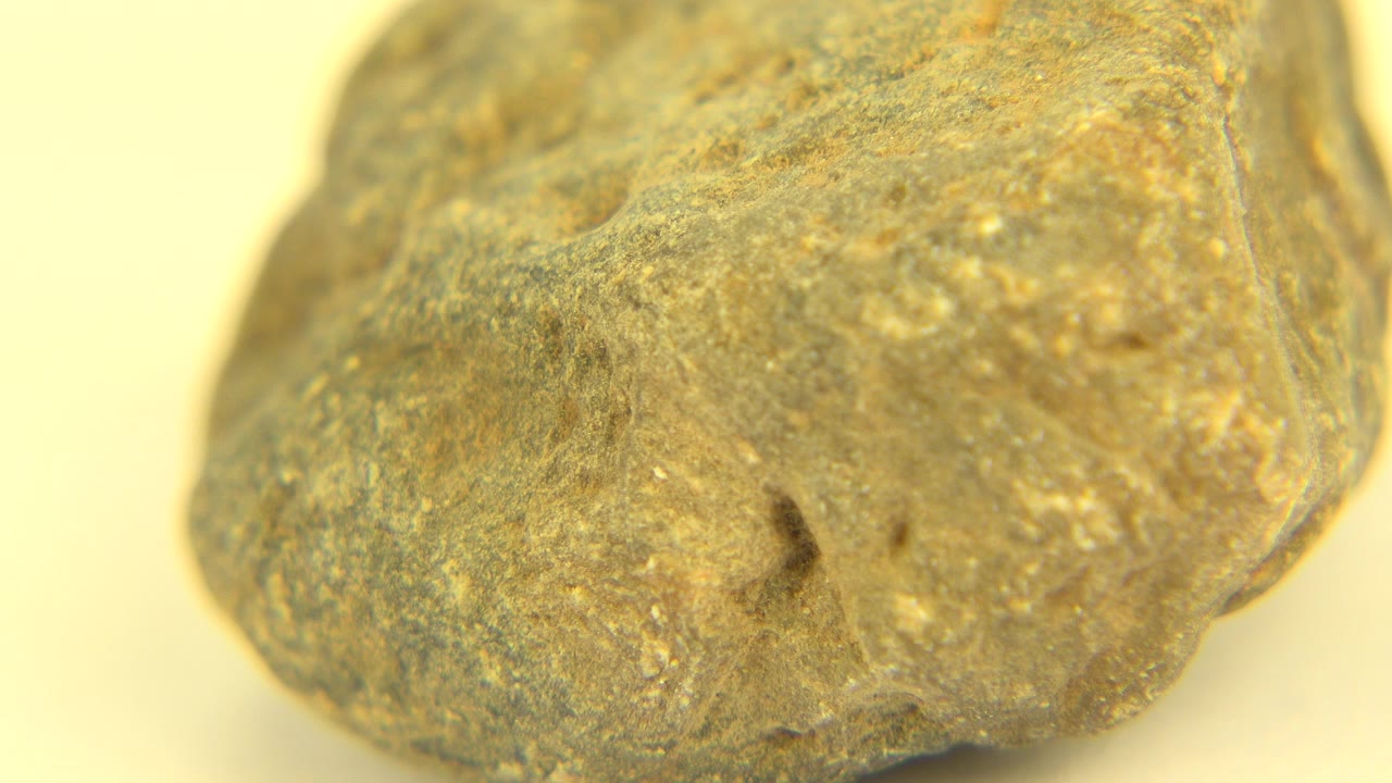 Close view of a rough orange, gray, and golden stone on a pale surface in Westminster, Colorado, with the left side prominent and no visible people.