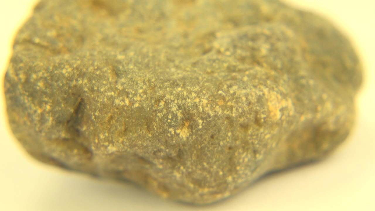 Second close-up frame shows the rock's front face with mottled grey-green color, golden flecks, shallow focus, and no visible people.