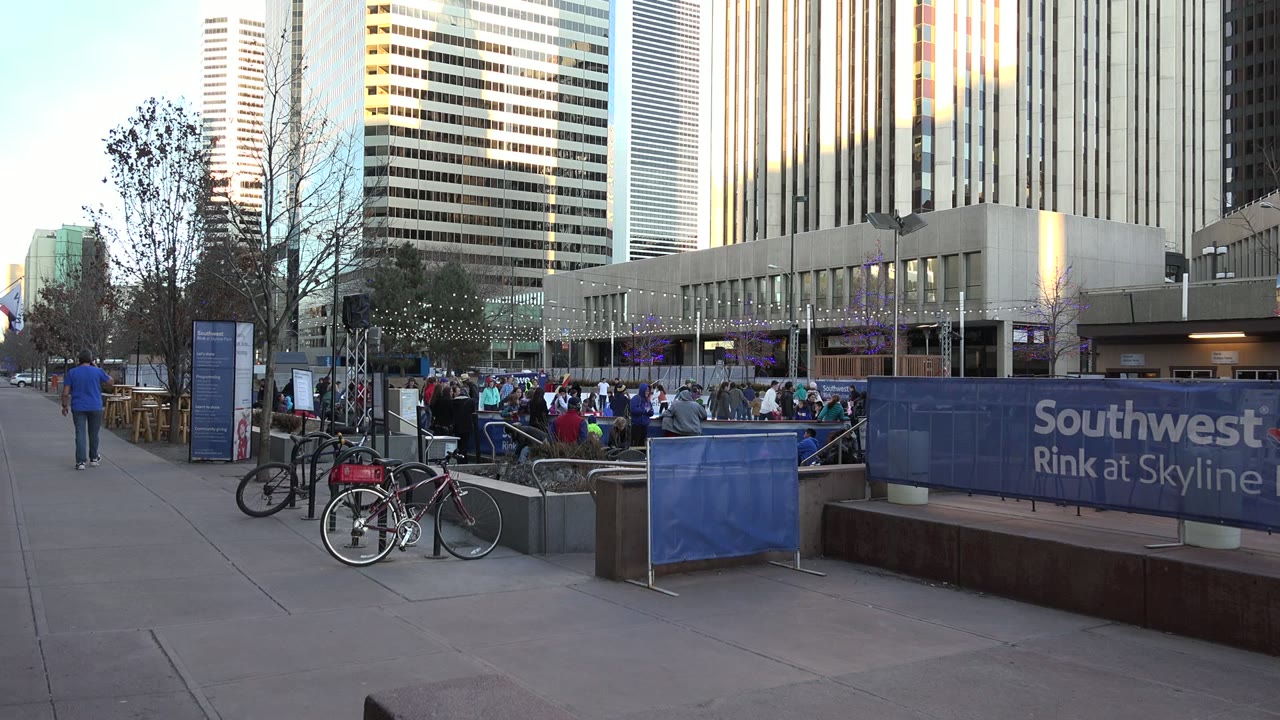 Second frame shows the Westminster rink from a similar ground view, with bicycles at left, spectators and skaters across the ice, blue barriers, and office towers filling the background.