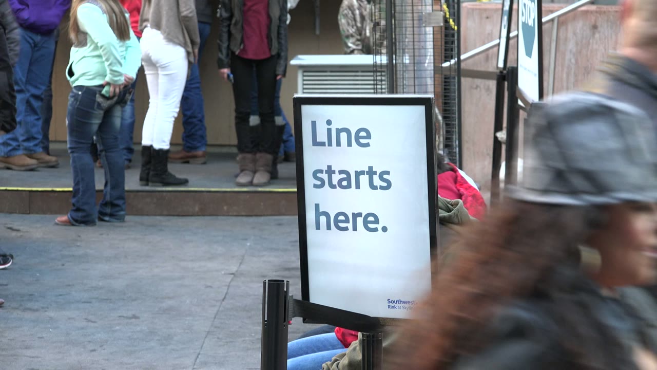 Line starts here sign beside people waiting outside an entrance.