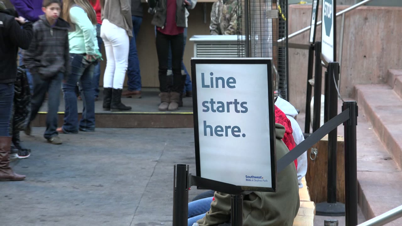 A blurred person passes close to the camera in Westminster, Colorado, partially obscuring the “Line starts here.” sign and people behind it.