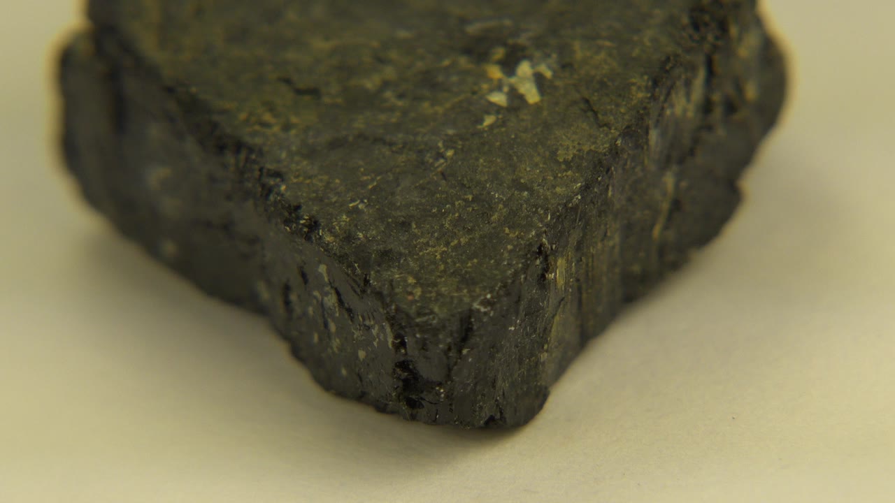 Close view of a dark rough rock on a pale surface in Westminster, Colorado, with the front point facing the camera and no visible people.