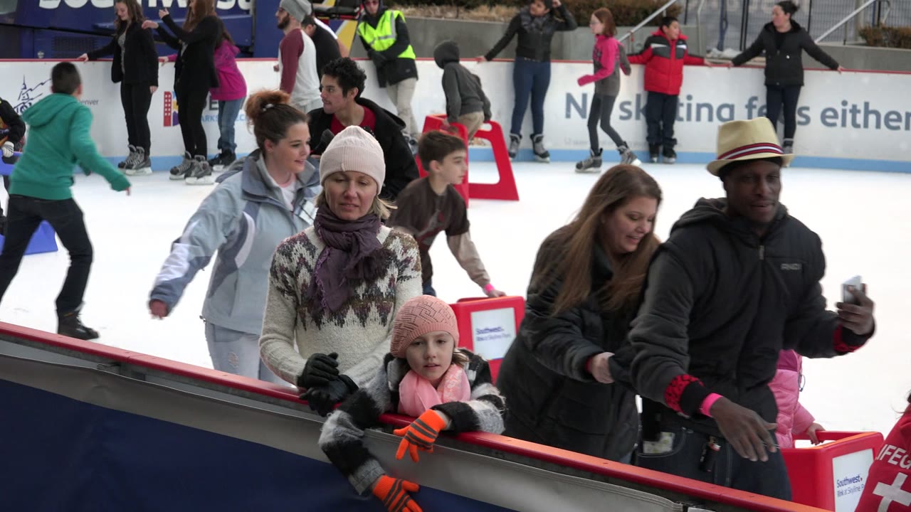 Adults and children skate past the boards on a crowded rink.