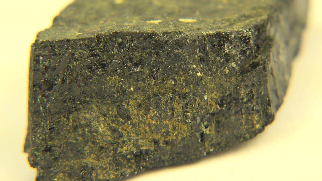 Opening close-up of a dark brown rough rock fragment in Westminster, Colorado footage, with a pale yellow background and no visible people.