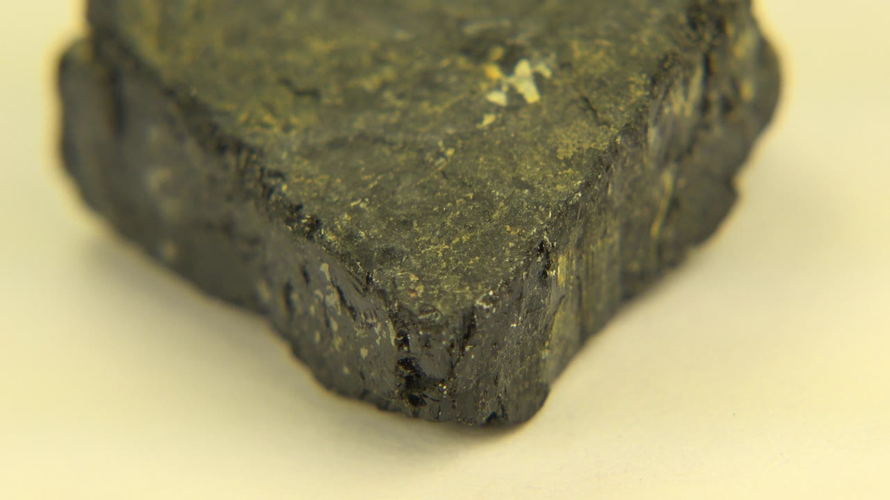 Close-up start of a dark rough rock on a cream tabletop in Westminster, Colorado, with shallow focus and no visible people.