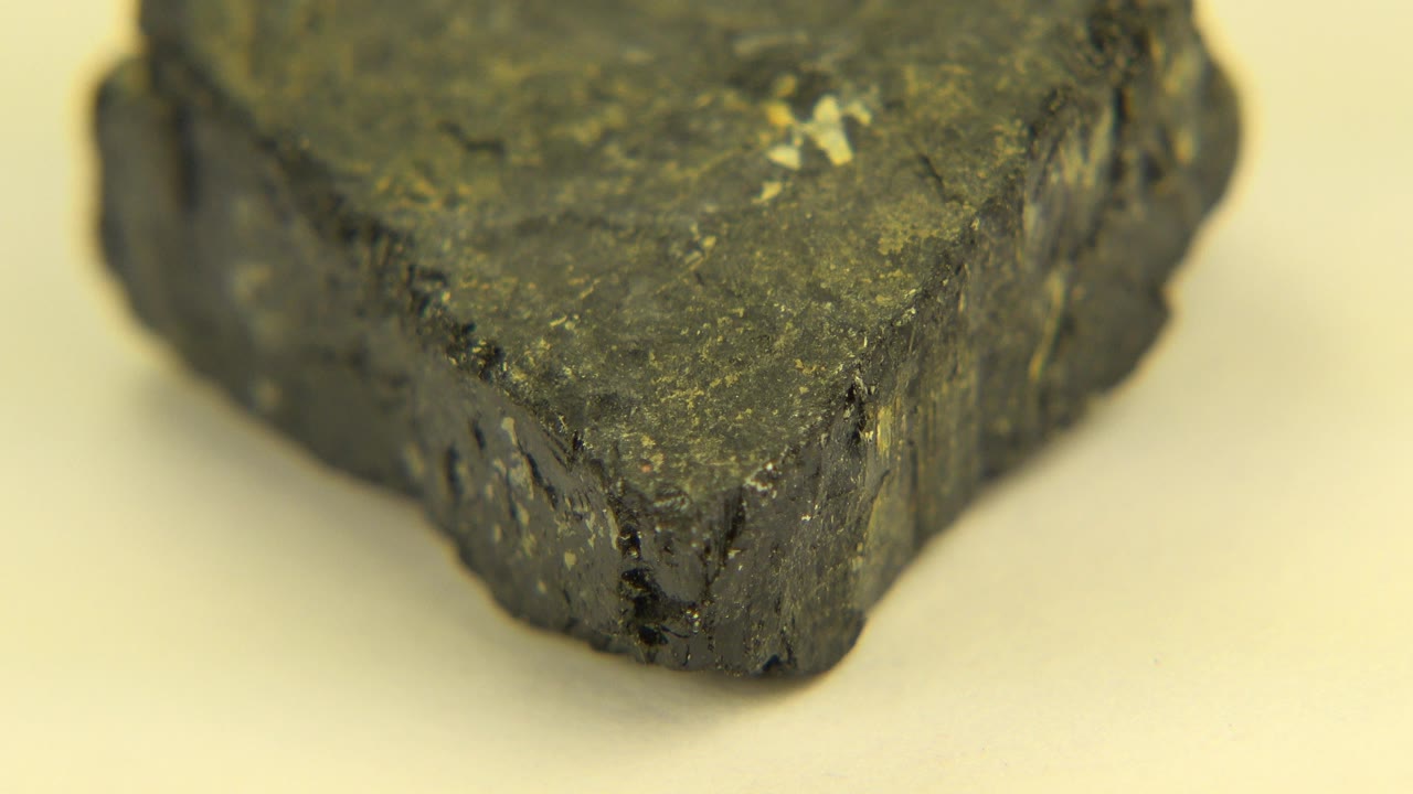 The dark rock appears slightly rotated on the cream tabletop, showing a front ridge and pale specks, with no visible people.